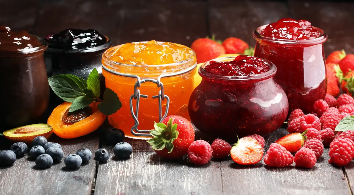 Jellies and Jams in jars on a table with fruit.