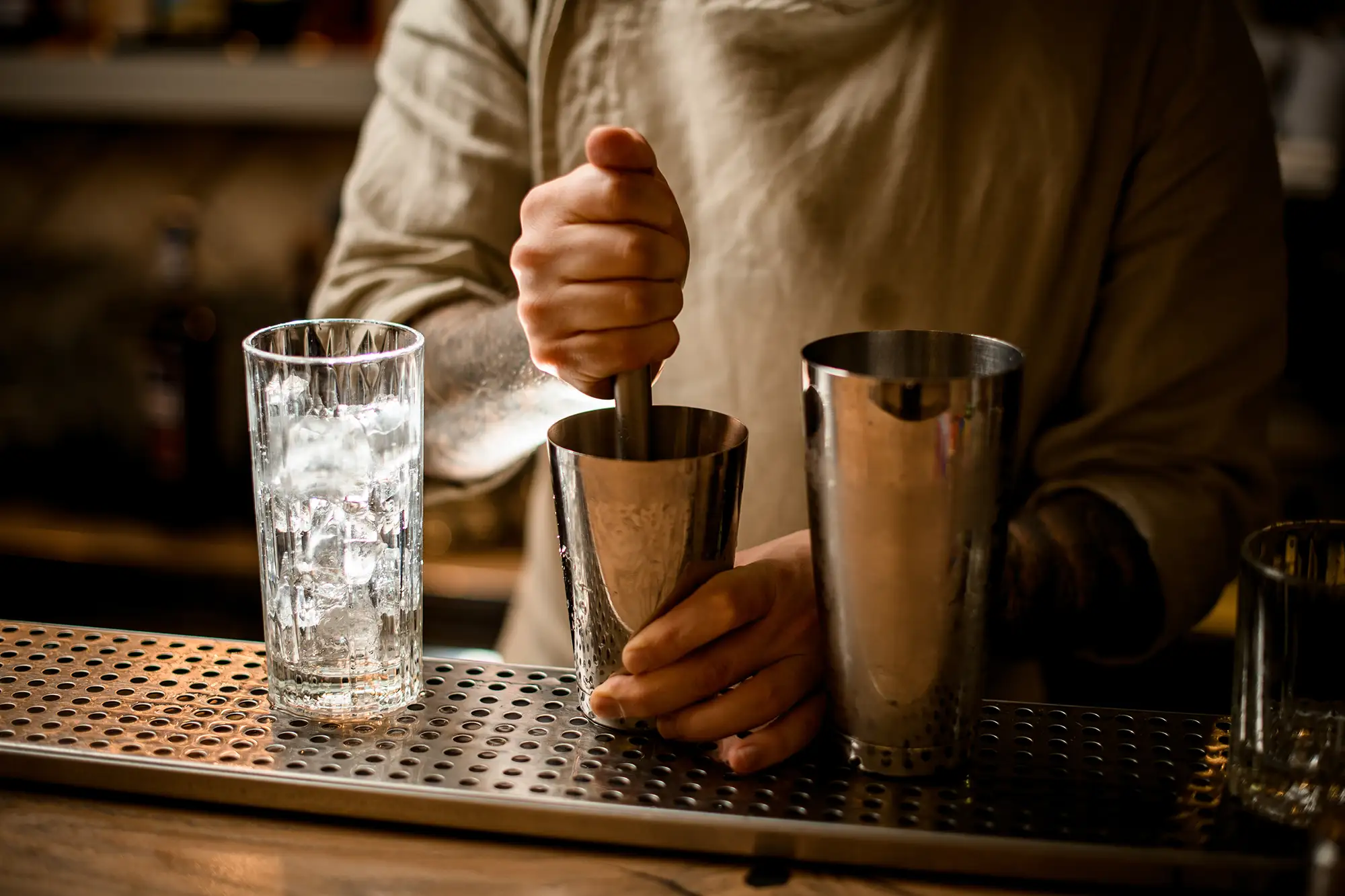 A bartender muddling ingredients in a part of a Boston shaker. A glass with ice is on the counter while the bartender presses the ingredients.