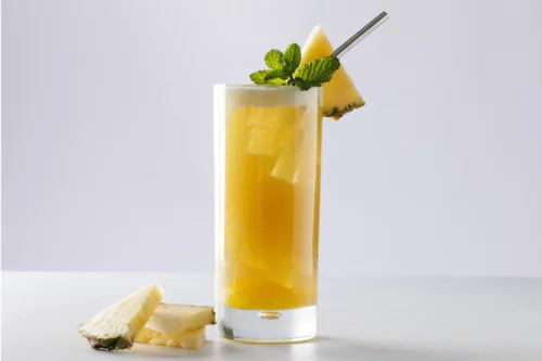 A pineapple yuzu tea with pineapple chunks and ice. It’s garnished with pineapple and mint. There are pineapple slices next to the glass.